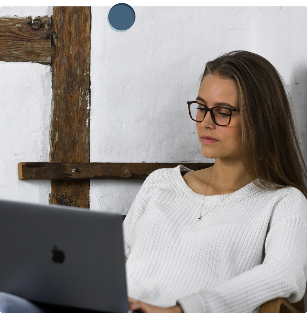 Jonge vrouw met witte trui en bril op haar gezicht zit op haar laptop te kijken